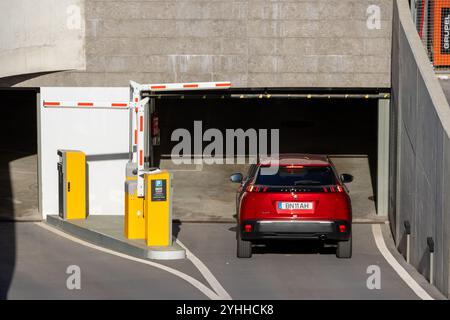 Auto rossa che entra nel garage sotterraneo passando attraverso la barriera aperta con terminale di pagamento Foto Stock