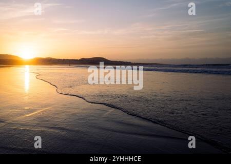Oceano ondulato e spiaggia contro le montagne al tramonto Foto Stock