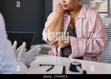 Primo piano di una donna afroamericana irriconoscibile affetta da psoriasi che punta all'eruzione cutanea sul gomito mentre si consulta con il dermatologo nello spazio di copia della clinica Foto Stock