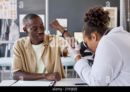 Ritratto di un uomo afroamericano sorridente che visita il medico con dermatologo che esamina la pelle usando il dermascope in clinica Foto Stock