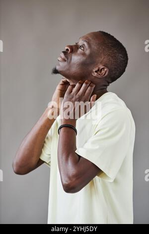 Immagine laterale minima di un uomo afroamericano adulto affetto da problemi di pelle che graffiano il collo su sfondo grigio in studio Foto Stock