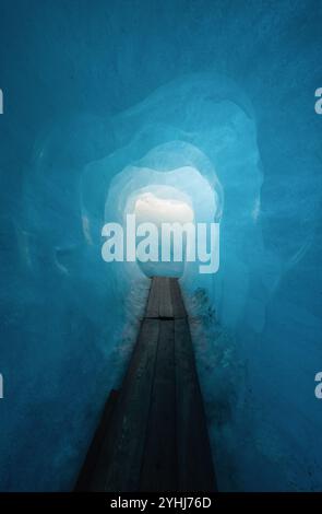 All'interno del ghiacciaio Rhône. Luce alla fine della grotta di ghiaccio blu. Passerella in legno nel tunnel all'interno di un ghiacciaio. Foto Stock