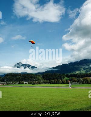 Parapendio in montagna. Il paracadutista si prepara ad atterrare sull'erba dell'aeroporto locale. Picco alpino di Stanserhorn sullo sfondo. Foto Stock