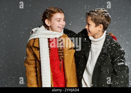 Due bambini sorridenti si godono una giornata invernale vestita con abiti caldi e colorati mentre i fiocchi di neve cadono. Foto Stock