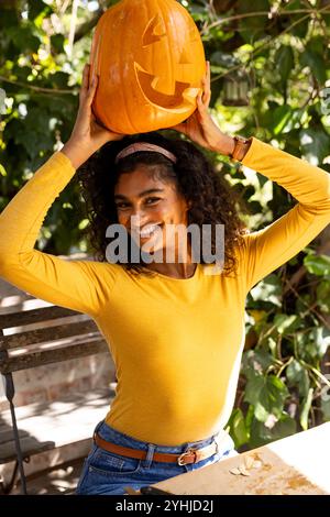 Halloween, donna sorridente che tiene la zucca scolpita in testa sul ponte, godendo della stagione natalizia Foto Stock