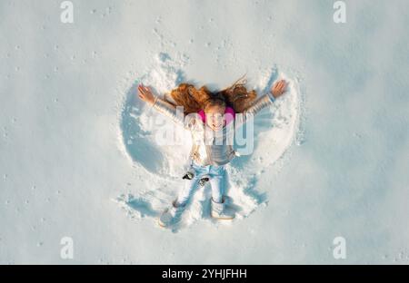 Angelo di neve fatto da un bambino nella neve. Bambino sorridente sdraiato sulla neve con spazio per la copia. Capretto divertente che fa l'angelo della neve. Foto Stock