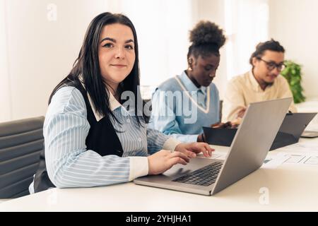 Gruppo eterogeneo di giovani professionisti che lavorano insieme in un moderno ufficio, concentrandosi sulle attività informatiche con un atteggiamento positivo Foto Stock