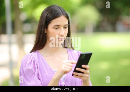 Donna seria che usa il cellulare in un parco verde Foto Stock