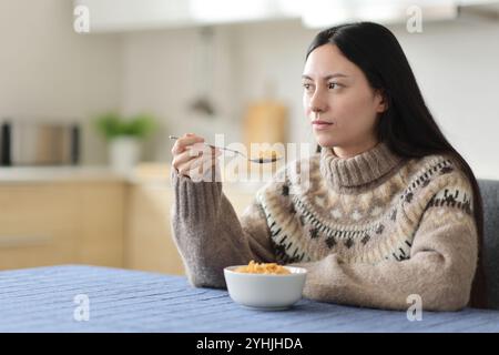 Donna asiatica seria in inverno che mangia cereali in cucina a casa Foto Stock