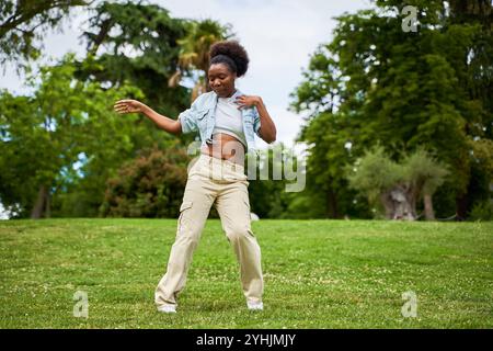 Una donna africana con i capelli ricci, indossa una giacca in denim, balla e si diverte, irradiando gioia ed energia nei suoi movimenti. Foto Stock