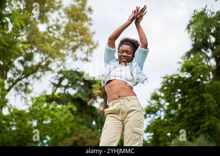 Una donna africana con i capelli ricci, indossa una giacca in denim, balla e si diverte, irradiando gioia ed energia nei suoi movimenti. Foto Stock