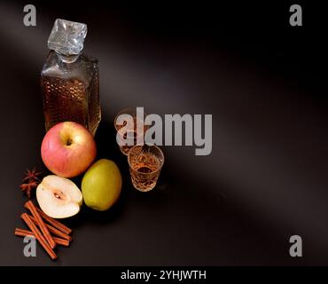 Liquore di mele con cannella e anice su sfondo nero, alcol fatto in casa in una ciotola di cristallo, frutta matura e spezie nelle vicinanze. Primo piano. Foto Stock