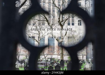 New York City, USA - 15 aprile 2017: Veduta dell'edificio della borsa valori americana attraverso una recinzione del cimitero. Foto Stock