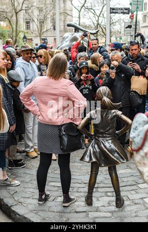 New York, USA - 15 aprile 2017: Una donna posa con la statua di Fearless Girl mentre una folla si riunisce per scattare foto. Foto Stock