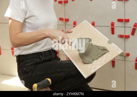 Donna che affianca le pareti del bagno, applica l'adesivo su una piastrella e posiziona la piastrella in ceramica nella giusta posizione. Processo di installazione delle piastrelle nel bagno Foto Stock