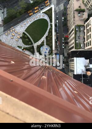 Vista aerea da un alto edificio che mostra un parco unico sul tetto con un prato di forma ovale e un'area salotto. La scena include vivaci strade cittadine. Foto Stock