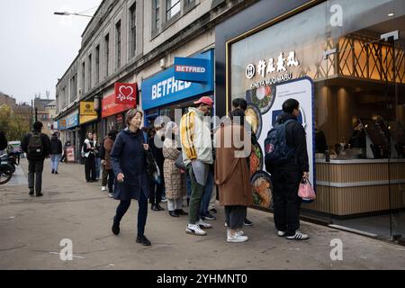 I giovani amanti dello shopping fanno la fila fuori da un ristorante di cucina coreana accanto a una filiale di BETFRED Wimbledon nel sud-ovest di Londra, Inghilterra, Regno Unito Foto Stock