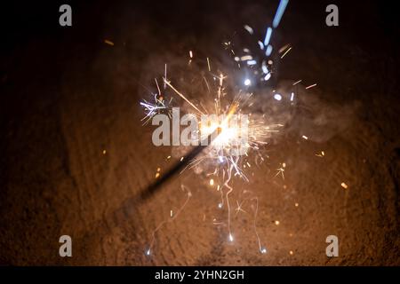 Un singolo sparkler brucia brillantemente su uno sfondo scuro, emettendo una pioggia di scintille luminose e fumo. Magia festiva per i festeggiamenti. Foto Stock