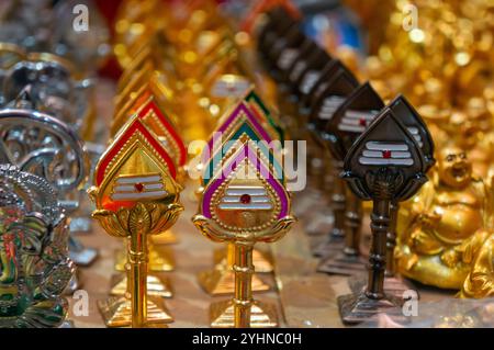 Colorati souvenir religiosi indù trishul in vendita in una bancarella del mercato. Foto Stock