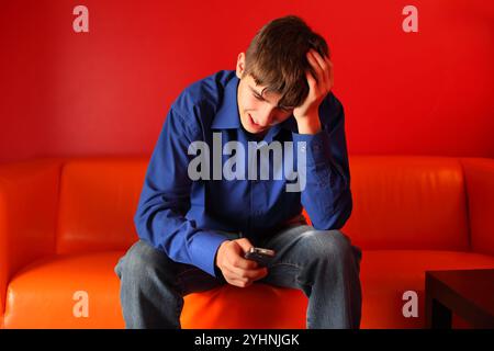 teenager triste seduto sul divano con il telefono cellulare Foto Stock