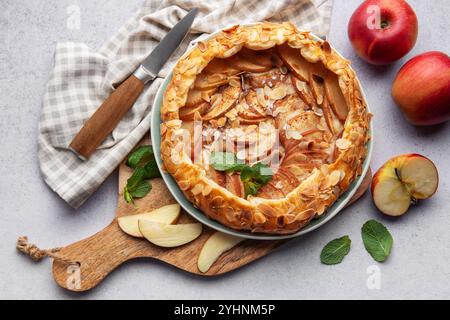 galette di mele appena sfornata decorata con scaglie di mandorle e menta, servita su un tavolo con mele fresche e un coltello Foto Stock