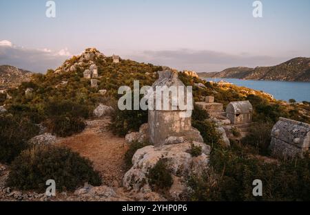 Sarcofago in pietra dell'antica città di Simena Kaleköy in Turchia. Mare Mediterraneo circondato da aspre colline elencate come luce mattutina. Trekking archeologico Foto Stock