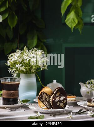 Biscotti a forma di uovo di Pasqua con mandorle e cioccolato su un tavolo con caffè, fiori e stoviglie, creando un'atmosfera accogliente in primavera Foto Stock