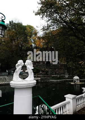 Un tranquillo giardino caratterizzato da un tranquillo laghetto, sculture ornate e lussureggiante fogliame autunnale. Le statue si stagliano in una pacifica riflessione, circondate da V Foto Stock