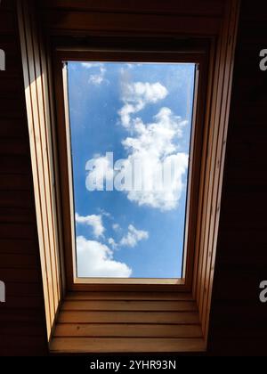 Una vista di un cielo blu luminoso con soffici nuvole bianche viste attraverso un lucernario di legno. L'immagine evoca sensazioni di pace e relax, offrendo un ser Foto Stock