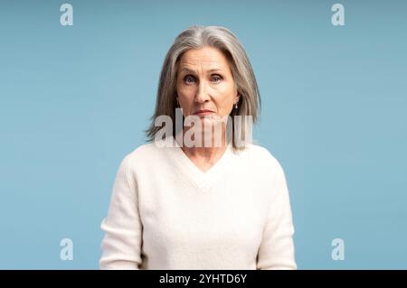 Ritratto di una donna dai capelli grigi triste e infelice che indossa abiti casual, guarda la macchina fotografica, posa isolata su sfondo blu Foto Stock