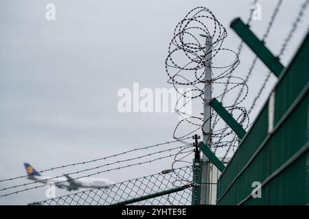 Sicherheitszaun mit Stacheldraht und Flugzeug im Hintergrund 12.11.24, Francoforte: Symbolfoto, Illustrationsbild, Symbolbild, Illustrationsfoto, Alltagsszene Sicherheitszaun mit Stacheldraht und Flugzeug im Hintergrund Ein hoch gesicherter Zaun mit Stacheldraht, der den Bereich um einen Flughafen umschließt. Im Hintergrund ist ein Lufthansa-Flugzeug zu erkennen, das im Anflug ist. . . Frankfurt Hessen Germania *** recinzione di sicurezza con filo spinato e aereo sullo sfondo 12 11 24, foto simbolo Francoforte, immagine illustrazione, immagine simbolo, foto illustrazione, recinzione di sicurezza per scena quotidiana W Foto Stock