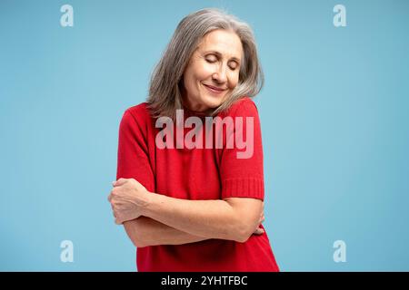 Ritratto di donna anziana sorridente che indossa abiti casual a occhi chiusi isolati su sfondo blu. Emozioni positive con Foto Stock