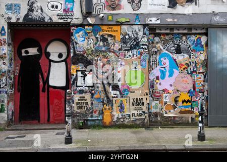 Street wall art Regno Unito. Raffigurando giocosamente due donne musulmane, una indossa la sua tradizionale Abaya nera e niqab e l'altra senza copertura facciale o copertura facciale bianca che permette solo agli occhi di vedere. Appena fuori Brick Lane, una porta del club circondata da graffiti. Opera dell'artista di graffiti Stik. Princelet Street, Tower Hamlets, East End Londra Inghilterra Regno Unito 2020s 2024 HOMER SYKES Foto Stock