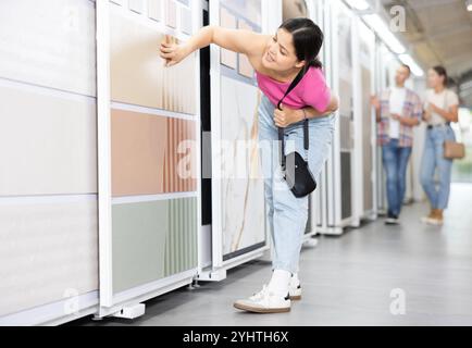 Donna asiatica che esamina campioni di piastrelle su espositore scorrevole in negozio Foto Stock