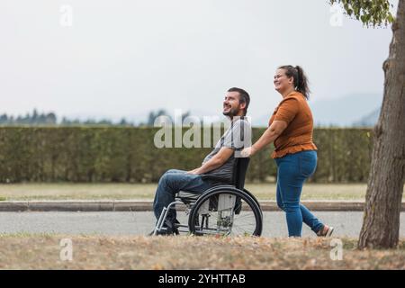 Un uomo sorridente, un utente in sedia a rotelle, e la sua assistente femminile che si diverte a praticare attività all'aperto. Concetto di supporto alla disabilità. Foto Stock