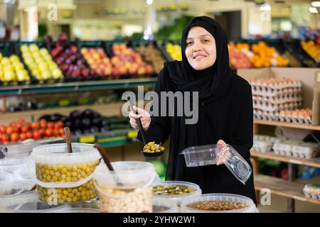 Giovane donna in hijab raccolta olive in supermercato Foto Stock