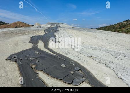 Paesaggio naturale caratterizzato da un flusso di fango incrinato da un piccolo vulcano attivo di fango sotto un cielo azzurro e un terreno arido (Vulcanii Noroiosi, Romania) Foto Stock