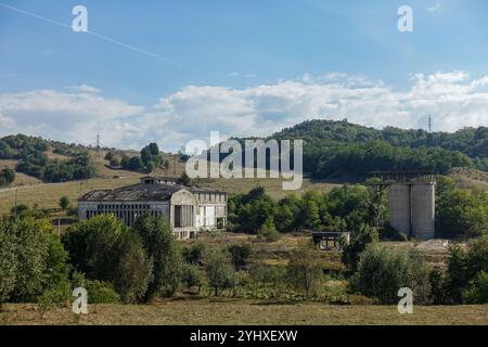 Vecchio edificio industriale abbandonato con finestre rotte e vegetazione sovrastata sotto un cielo blu in un ambiente rurale vicino a Câmpulung, in Romania Foto Stock