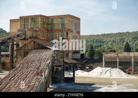 Vecchio complesso industriale abbandonato con strutture metalliche arrugginite e mucchi di minerali bianchi sopra la miniera di sale Salina Slanic, Romania Foto Stock