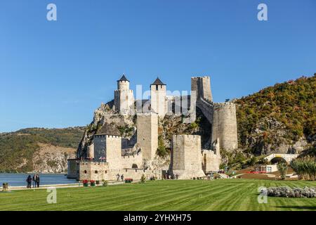 Fortezza medievale di Golubac con torri multiple su una collina rocciosa accanto a un fiume sotto un cielo azzurro, circondato dai verdi paesaggi del Danubio Foto Stock