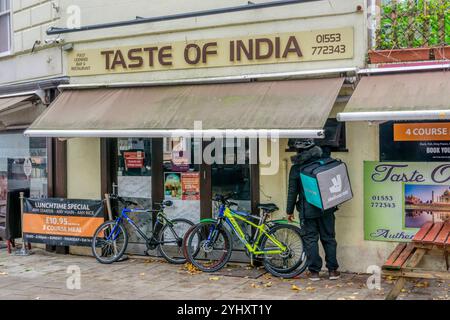 Un corriere di cibo Deliveroo presso un ristorante indiano da asporto a King's Lynn, Norfolk. Foto Stock