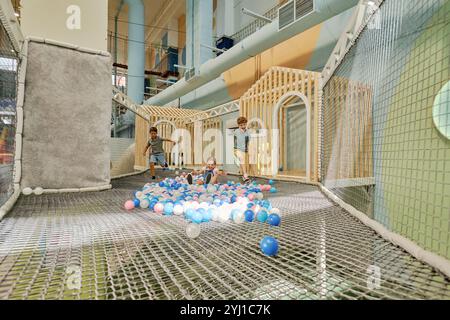 Tre bambini simpatici e entusiasti che corrono lungo il parco giochi con palloncini di vari colori mentre trascorrono del tempo insieme Foto Stock