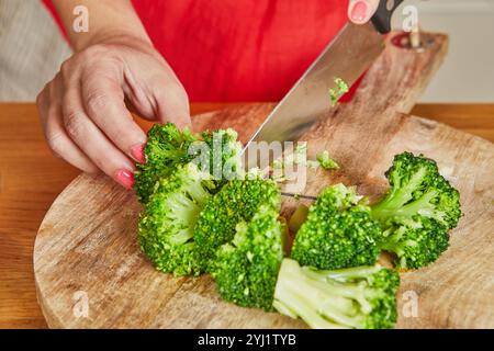 Una mano trita fiori di broccoli freschi su un tagliere di legno, preparando gli ingredienti per un pasto sano. Foto Stock