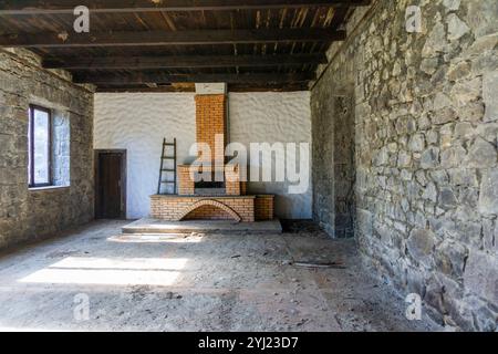 Caminetto in mattoni arancioni nella sala di una vecchia cantina abbandonata. Pareti in pietra, grandi finestre, soffitto in legno Foto Stock