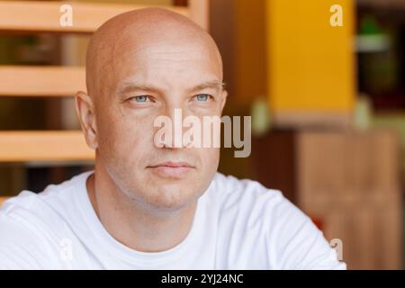 Un uomo calvo con un occhio blu fissa la telecamera. Sta indossando una camicia bianca. Concetto di solitudine e introspezione Foto Stock