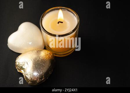 Una candela ardente con dolci a forma di cuore su sfondo scuro che creano un'atmosfera calda e romantica. Foto Stock