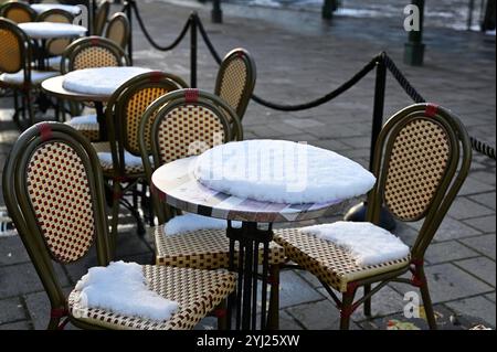 L'immagine mostra un'ambientazione da caffè all'aperto ricoperta di neve, con sedie vuote e tavoli spolverati di neve fresca. La caffetteria si trova su un'area pavimentata, e Foto Stock