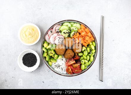 Poke hawaiano con riso, falafel, fagioli edamame verdi, avocado, pomodori ciliegini e hummus su sfondo grigio, vista dall'alto. Foto Stock