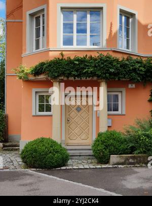 Casa arancione in una piccola città. Edificio compatto con porta d'ingresso al primo piano e balcone vetrato. Foto Stock