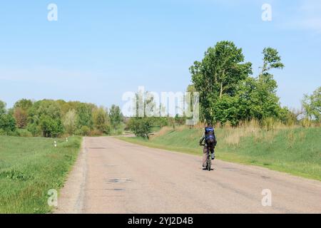 Un ciclista solitario con uno zaino cavalca una mountain bike in una giornata estiva di sole su un percorso ciclabile in autostrada. Foto di viaggio, attività estive. Foto Stock